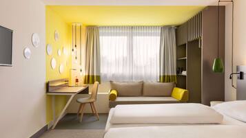 A hotel room with a desk, a sofa, two beds, a TV, and a window with curtains.