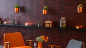Uma área de estar moderna com duas poltronas de baloiço, uma mesa redonda pequena e uma estante com objetos decorativos e plantas.