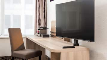 Ein Hotelzimmer mit Flachbildfernseher an der Wand, einem Holztisch mit Stuhl und einer Fernbedienung auf dem Tisch.