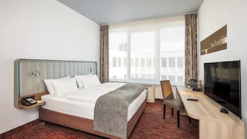 Ein Hotelzimmer mit Bett, Schreibtisch, Sessel, Fernseher und einem Fenster mit Vorhängen.