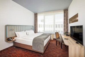 Et hotelværelse med en seng, et skrivebord, en stol, et fjernsyn og et vindue med gardiner.