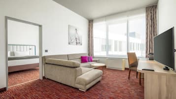 Ein Hotelzimmer mit Bett, Sofa, Fernseher und einem Fenster mit Vorhängen.