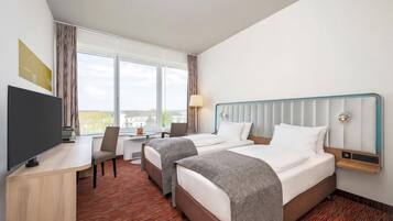 A hotel room with two beds, a desk, a chair, a TV, and a window with a view of buildings.