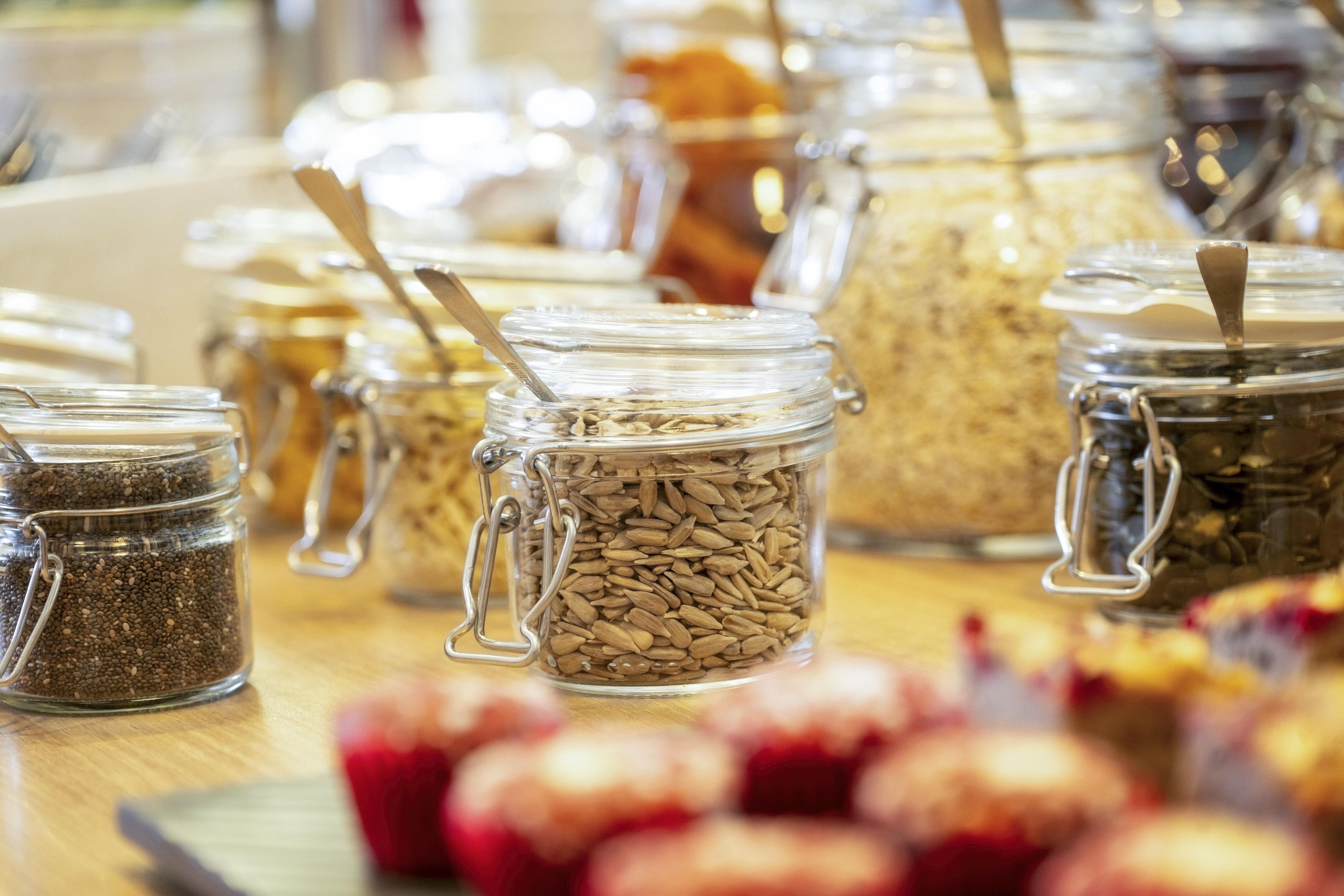 A variety of food items in glass jars with metal clasps, some with spoons inserted, on a wooden surface.