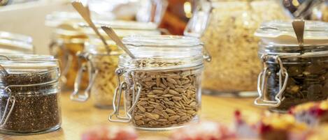 A variety of food items in glass jars with metal clasps, some with spoons inserted, on a wooden surface.