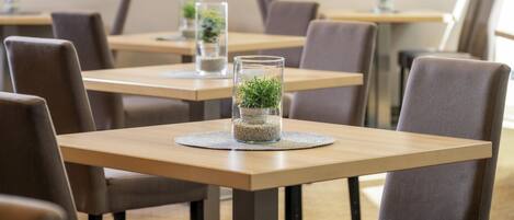 A dining area with square tables and chairs, each with a glass container holding a plant.