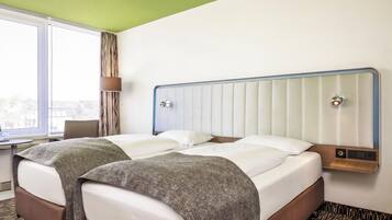 A hotel room with a bed, a desk, and a window.