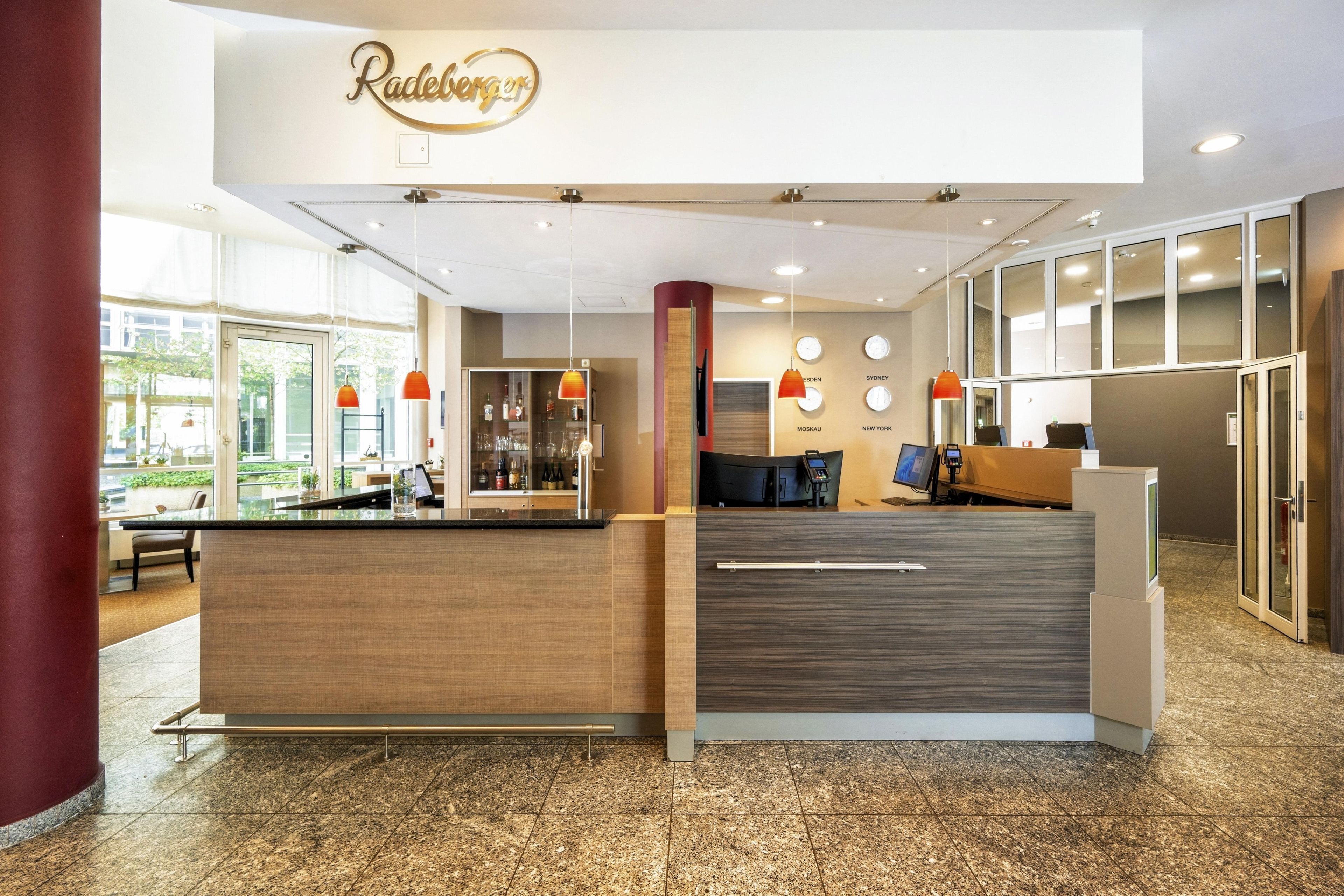 A reception area with a wooden reception desk, a glass display case with bottles, and a wall with clocks and city names.