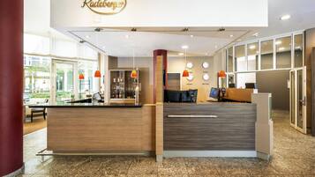 A reception area with a wooden reception desk, a glass display case with bottles, and a wall with clocks and city names.