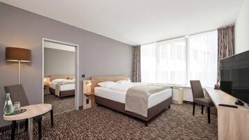 A hotel room with a bed, a desk, a chair, a TV, and a window with curtains.