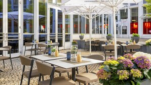 Un café al aire libre con mesas y sillas, sombrillas grandes y plantas en macetas.
