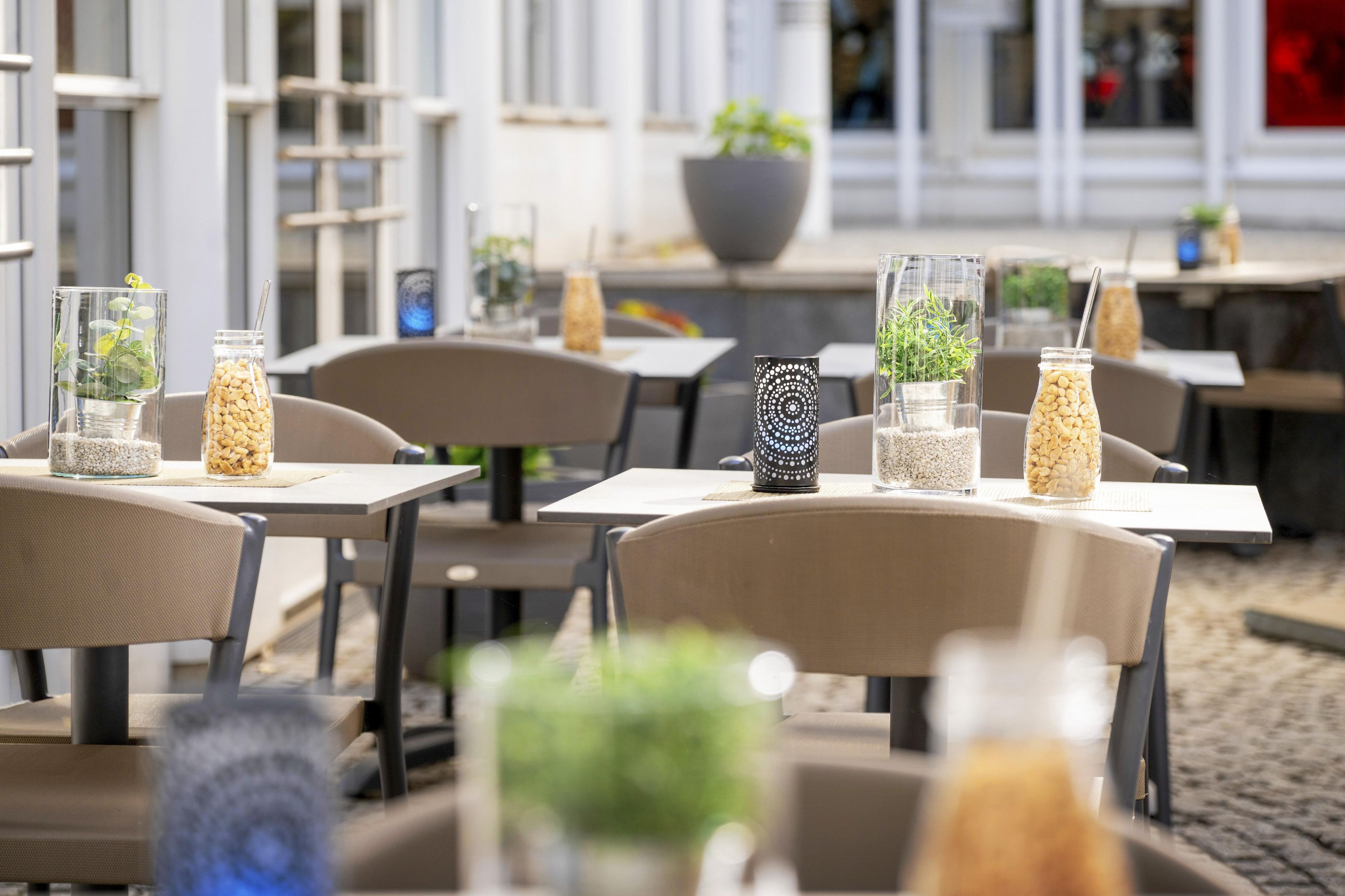 Ein Straßencafé mit Tischen, Stühlen und dekorativen Glasvasen mit Pflanzen.