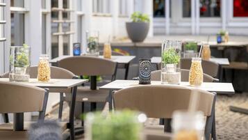 Ein Straßencafé mit Tischen, Stühlen und dekorativen Glasvasen mit Pflanzen.
