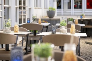 An outdoor cafe setting with tables, chairs, and decorative glass vases with plants.