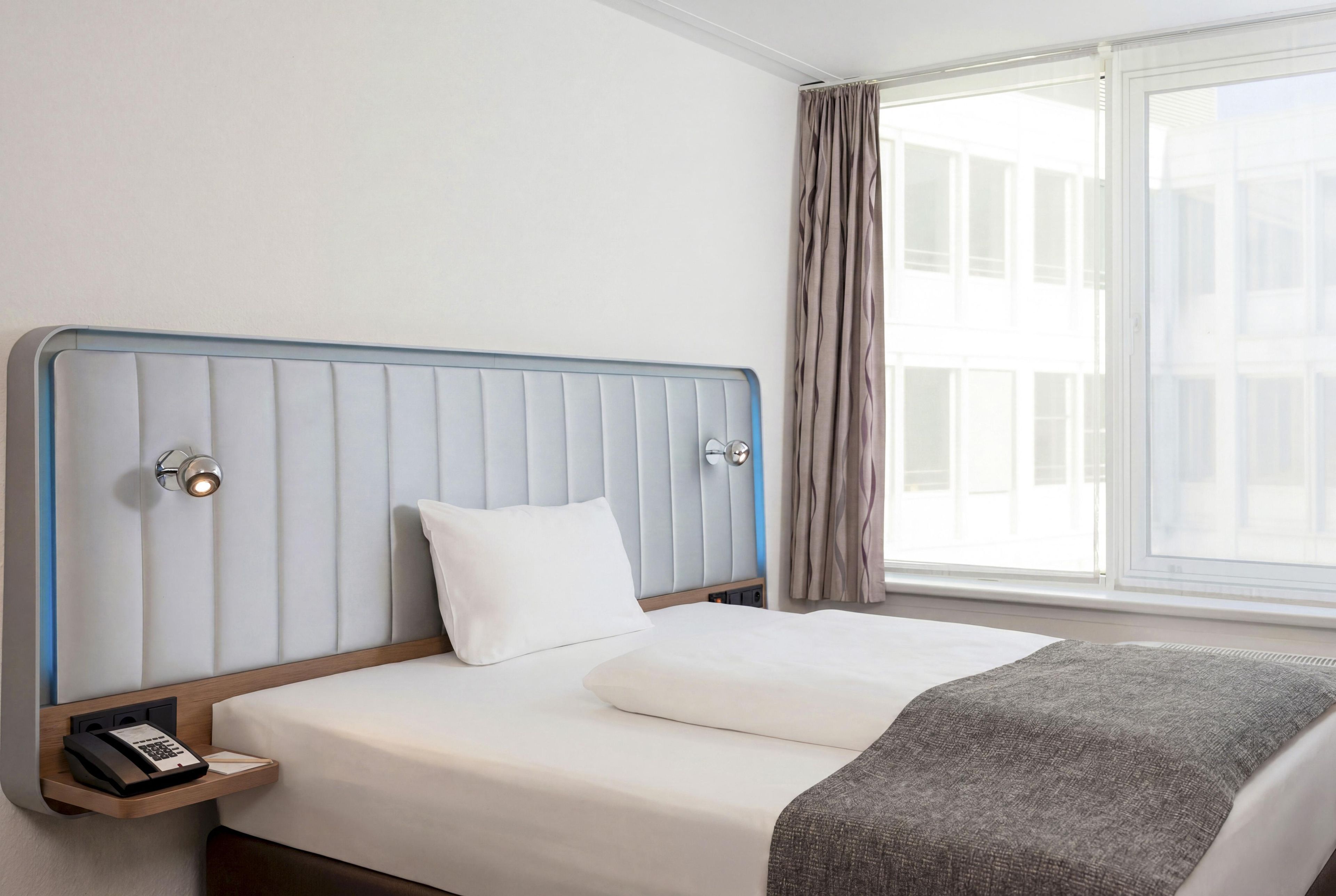 Ein Hotelzimmer mit Bett, Nachttischtelefon und einem Vorhangfenster.