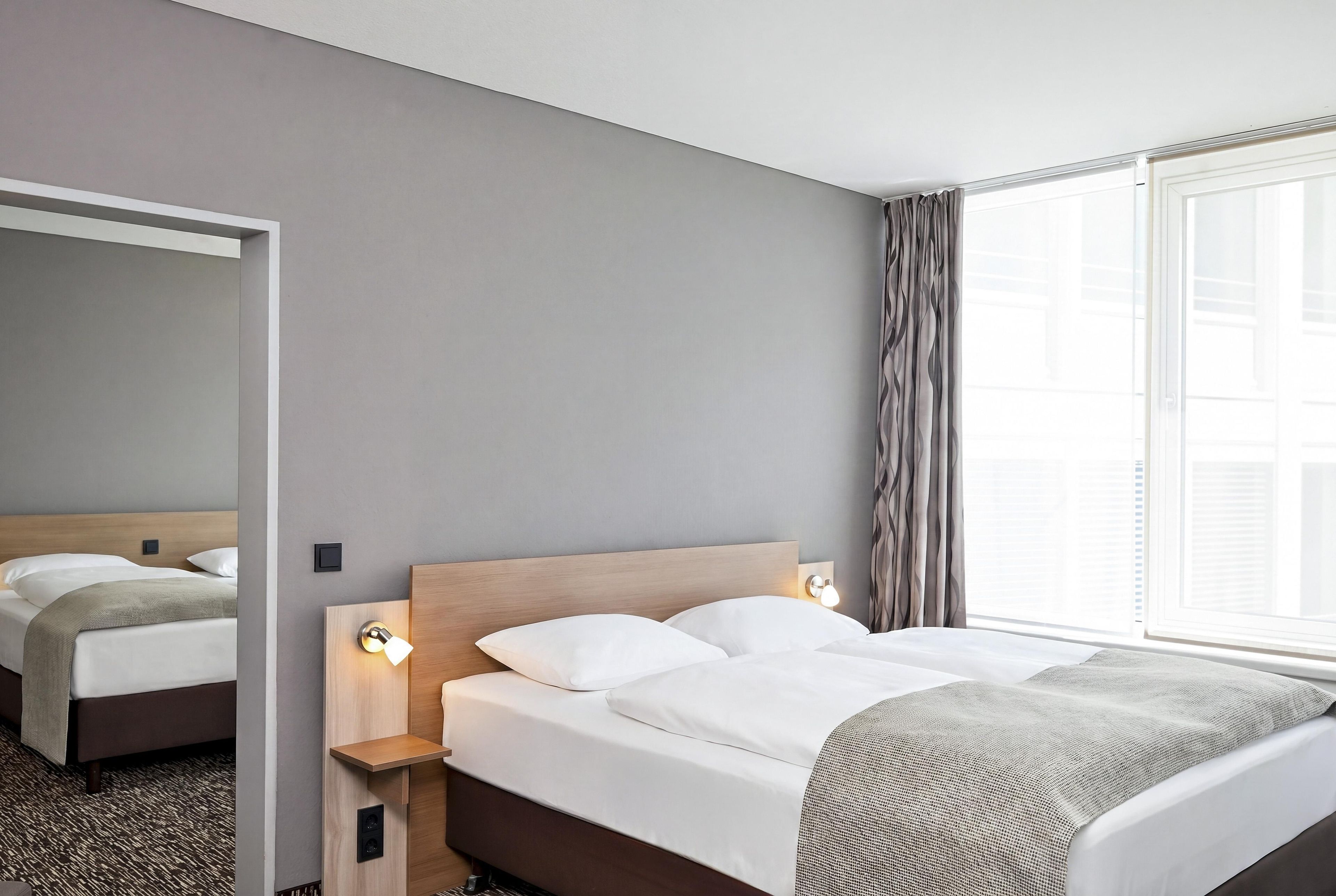 Een hotelkamer met een bed, nachtlampjes, een spiegel en een raam met gordijnen.