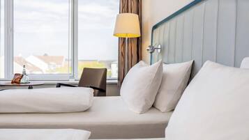 Ein Hotelzimmer mit Bett, Stuhl, Lampe und Blick ins Freie.