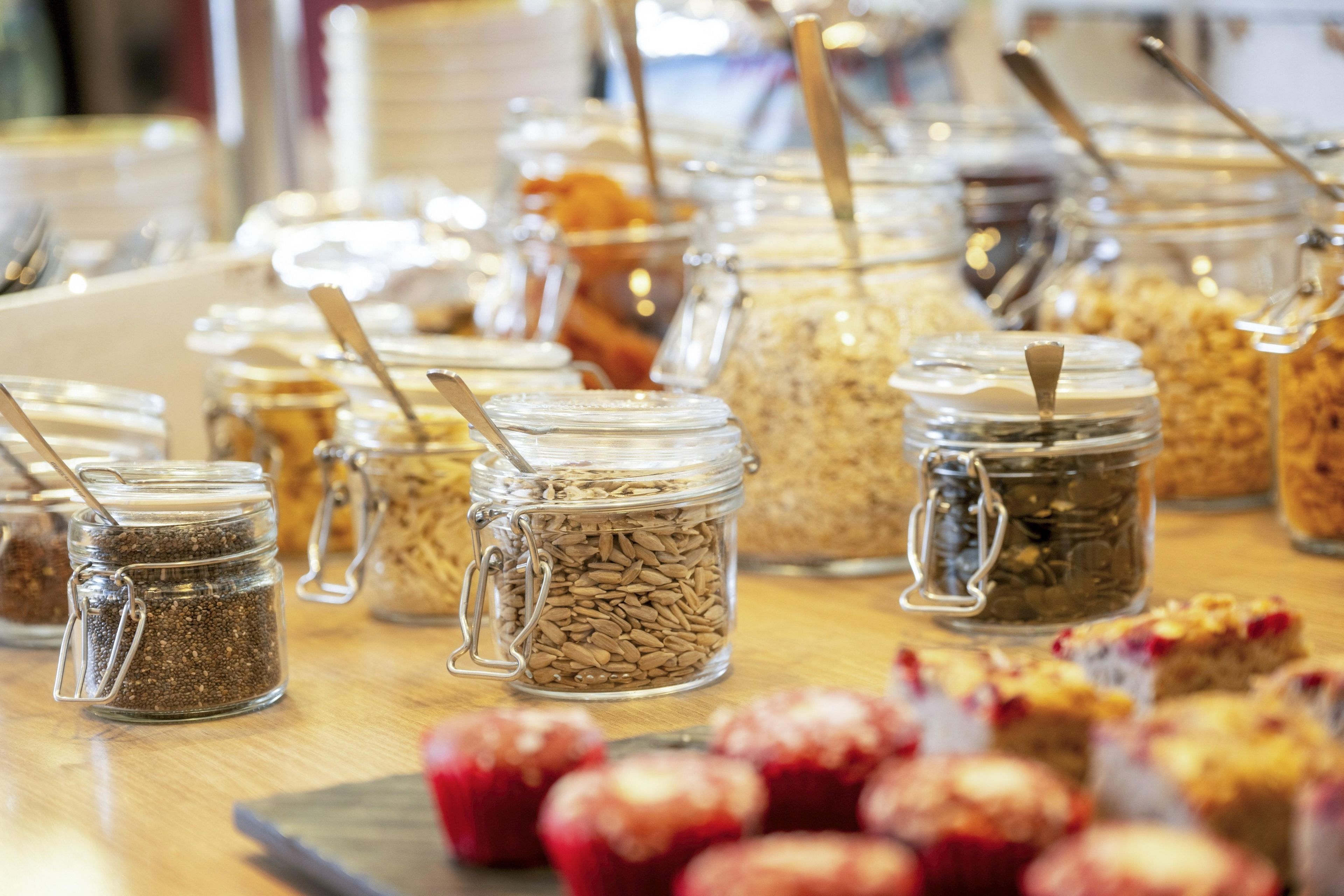 A variety of food items in glass jars with metal clasps and spoons, arranged on a wooden table.