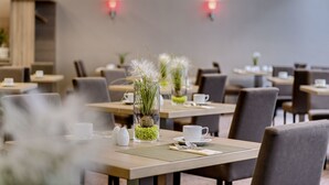 A dining area with tables set for two, featuring clear glass vases with plants and white cups.