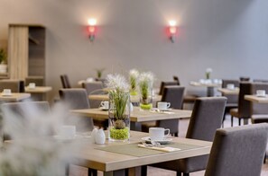Een eetgedeelte met tafels voor twee personen, met transparante glazen vazen met planten en witte kopjes.