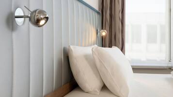 A hotel room with a bed, white pillows, a headboard with vertical lines, and wall-mounted lights.