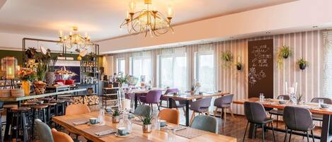 Un restaurante con varias mesas, sillas y una zona de bar con estanterías y plantas.