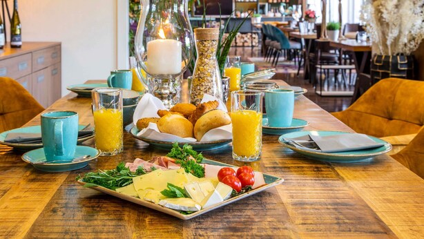 A breakfast setting with a variety of food items, including cheese, tomatoes, and pastries, on a wooden table. - Mercure Hotel Bad Oeynhausen City (Bad Oeynhausen)