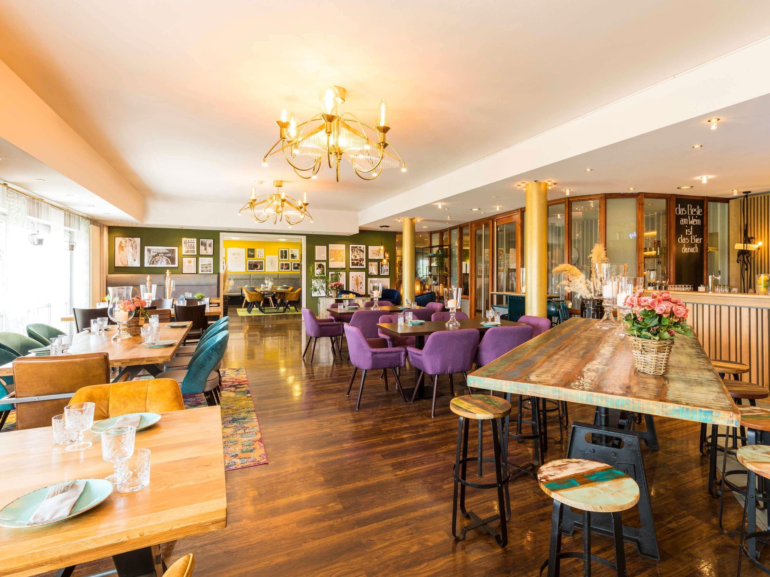 Interior de restaurante con mesas de madera, sillas moradas y una zona de bar.