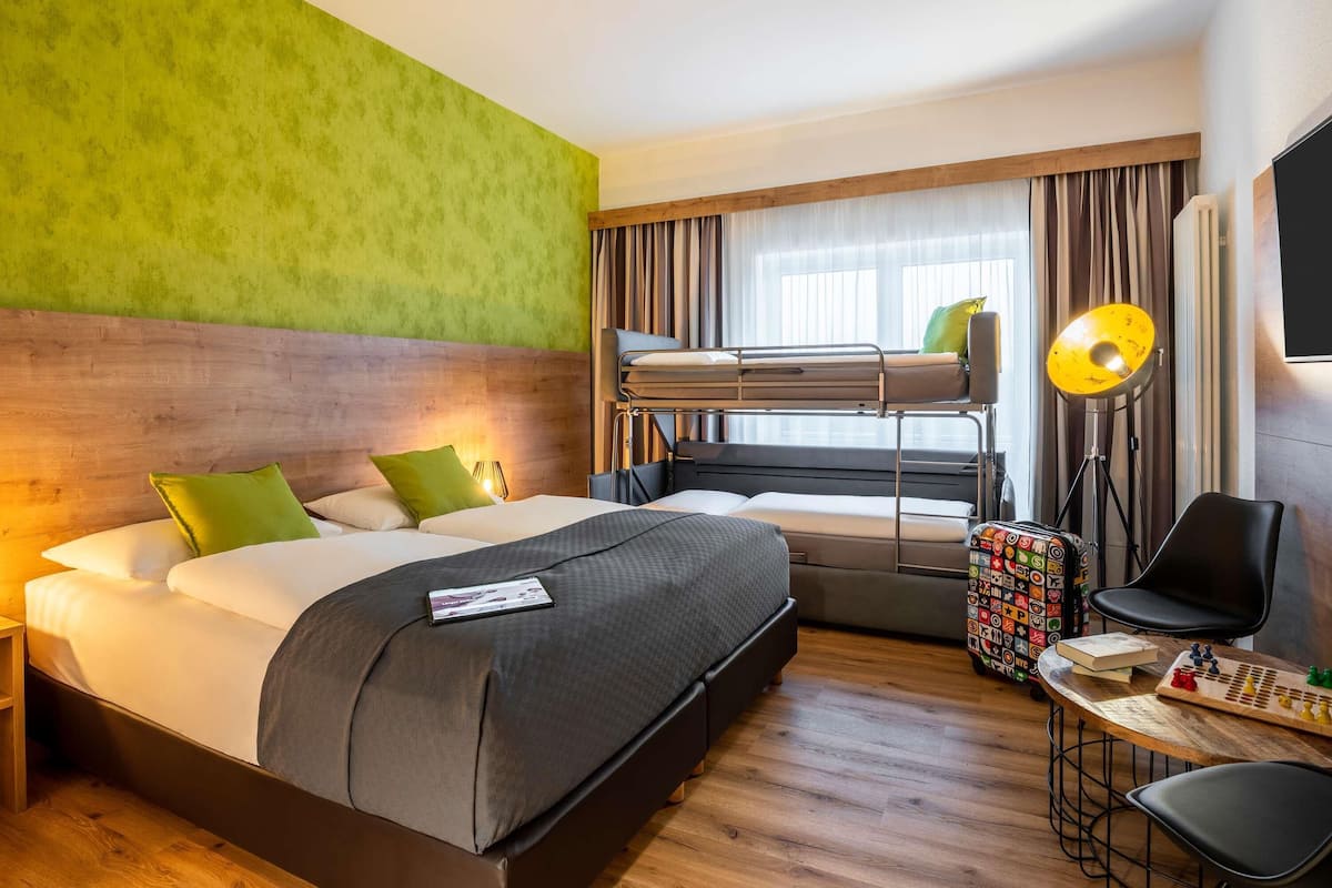 A hotel room with a bunk bed, a desk with a chessboard, and a lamp.