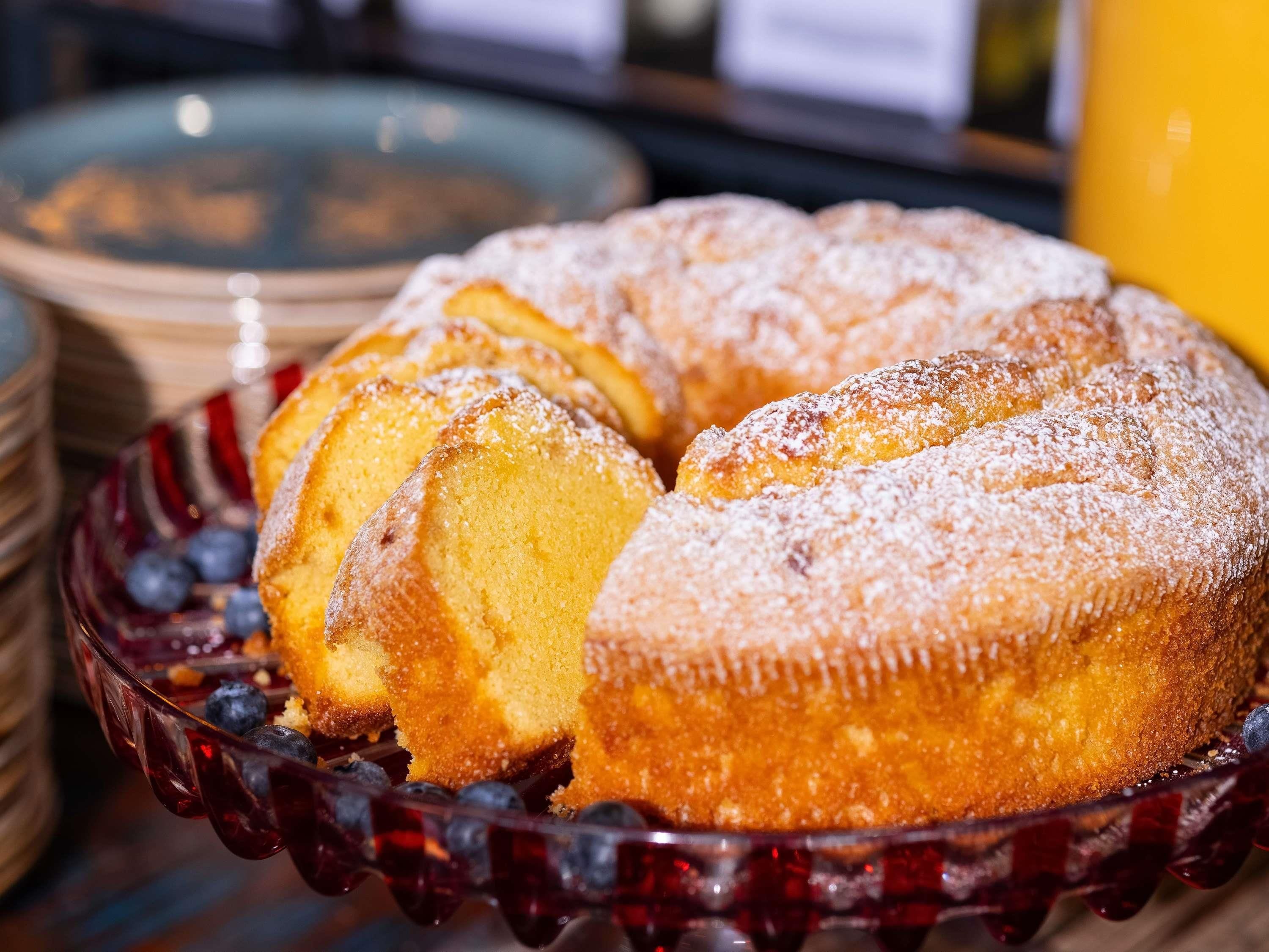Un gâteau en forme de couronne, présenté sur une assiette en verre, et garni de myrtilles.