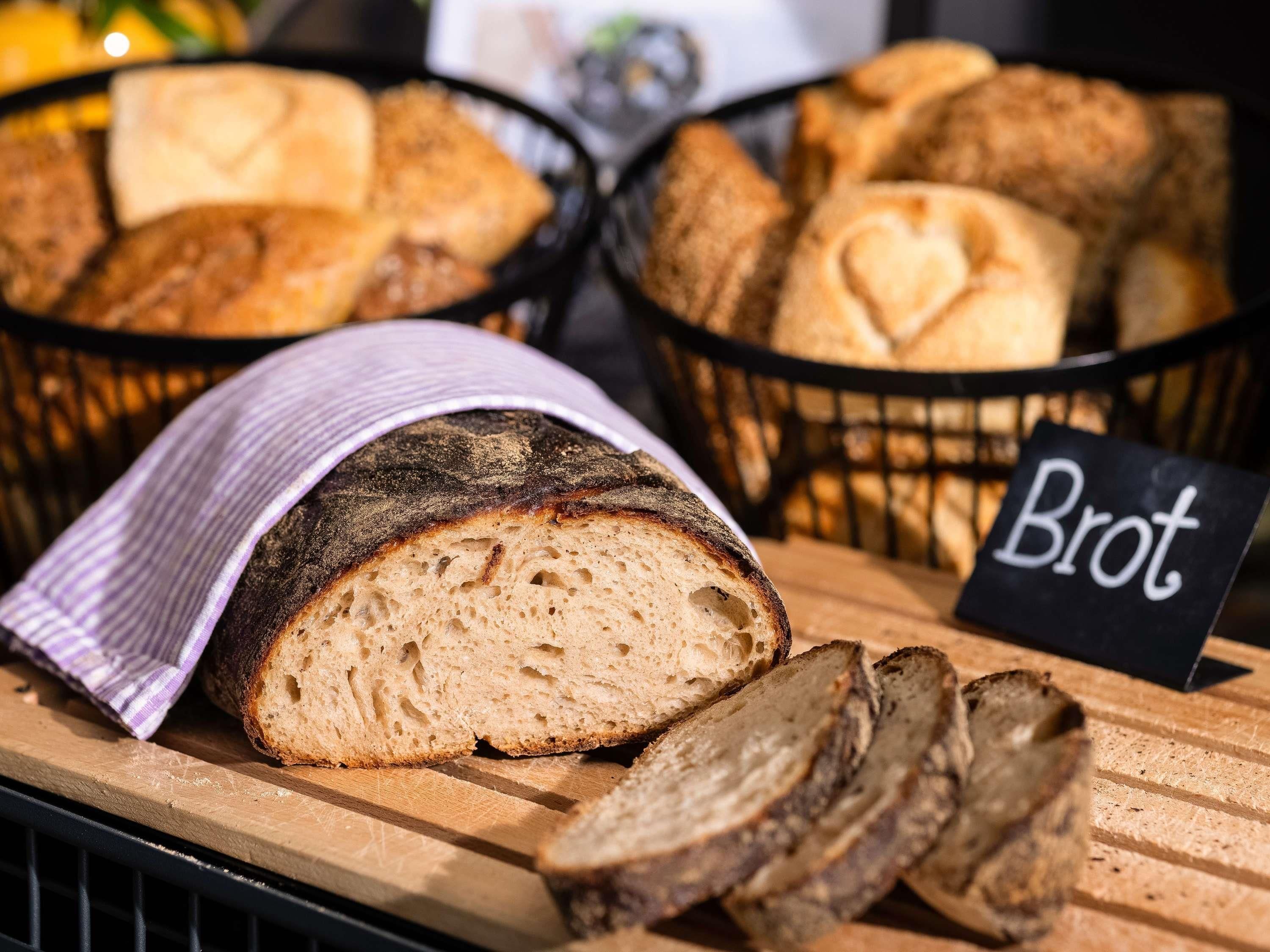 Une miche de pain étiquetée « Brot » sur une planche à découper, avec des tranches et des miches entières dans des paniers.