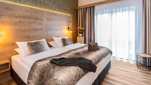 A hotel room with a large bed, wooden headboard, a small table, and a view of the city through the window. - Mercure Hotel Bad Oeynhausen City (Bad Oeynhausen)