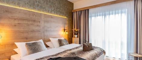 Habitación de hotel con una cama grande, cabecera de madera, una mesita y vistas a la ciudad por la ventana.