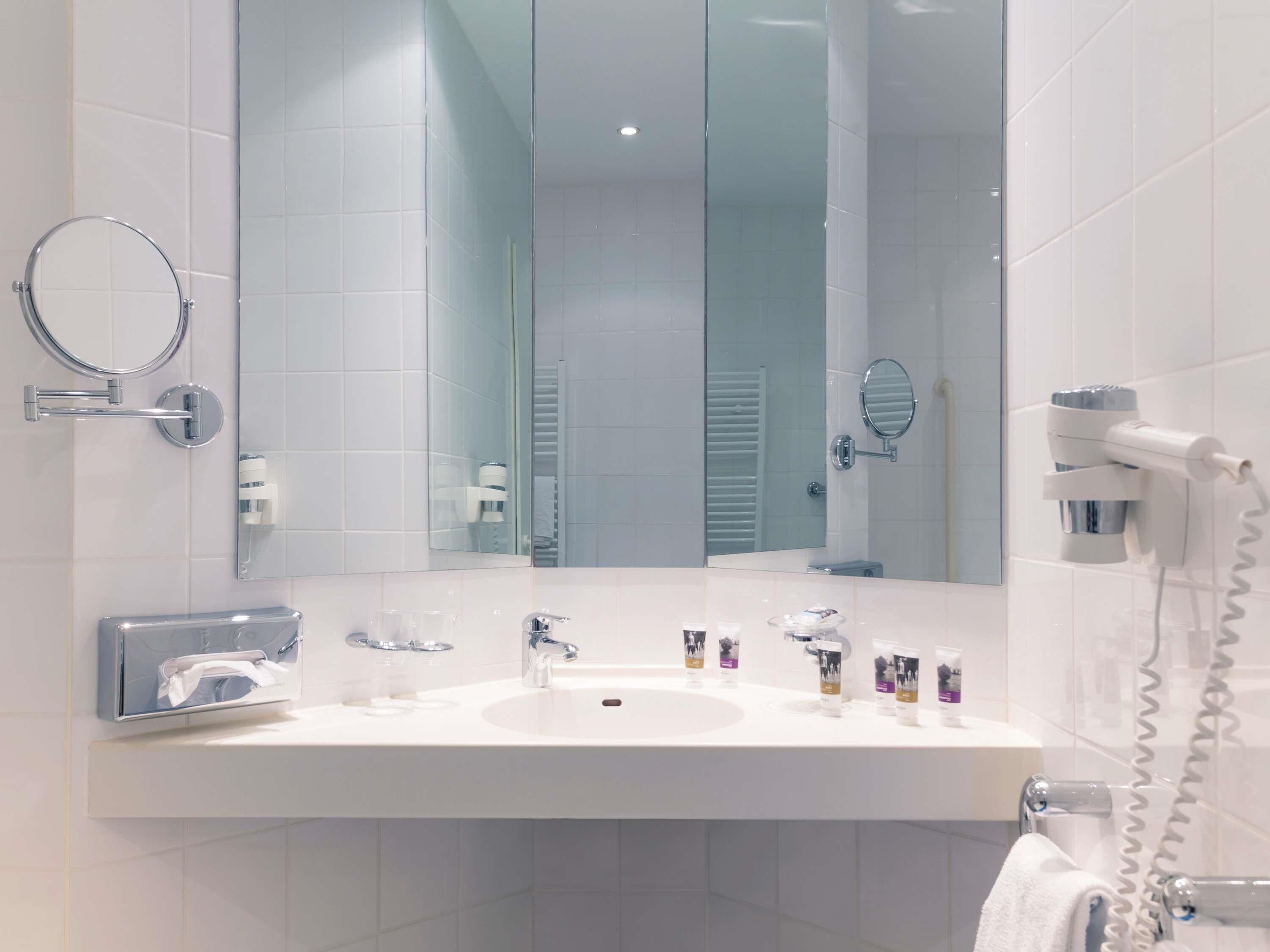 A modern bathroom with a large mirror, a white sink, and a hairdryer on the wall.