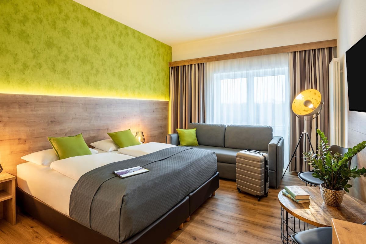 A hotel room with a bed, a sofa, a desk, a lamp, and a plant.