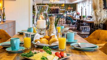 A breakfast setting with a plate of cheese, tomatoes, and herbs, a glass of orange juice, and a candle centerpiece.