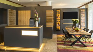 A modern reception area with a central desk, a bookshelf, and a dining area with chairs and a table. - Mercure Hotel Bad Oeynhausen City (Bad Oeynhausen)