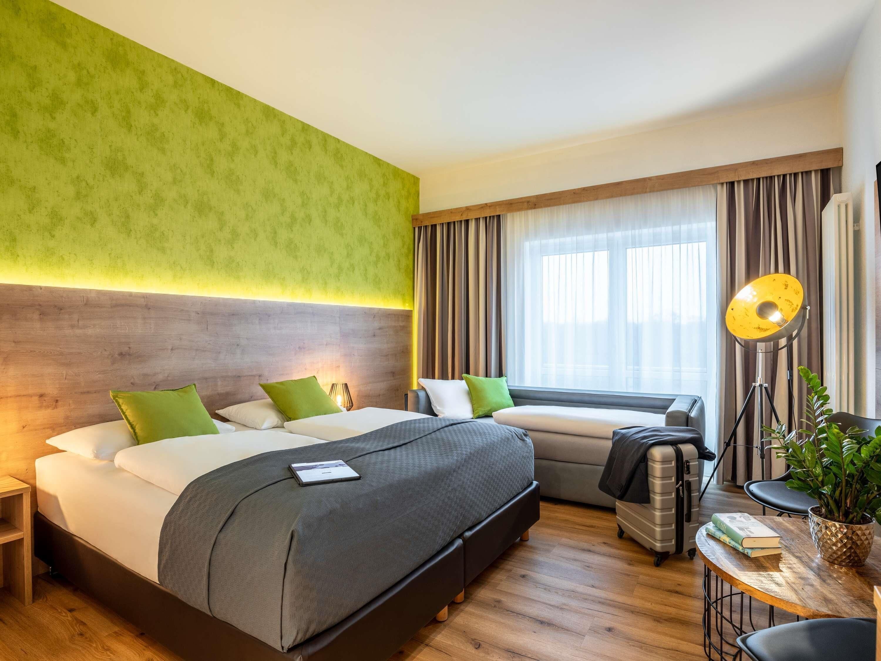 A hotel room with a bed, bedside table, lamp, and a view of the outdoors.