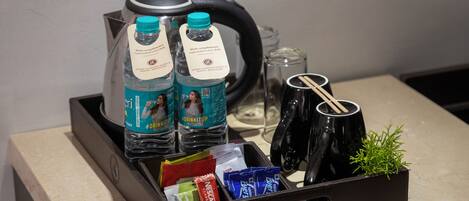 A tray with a kettle, two water bottles, a glass, a small plant, and various packaged items.