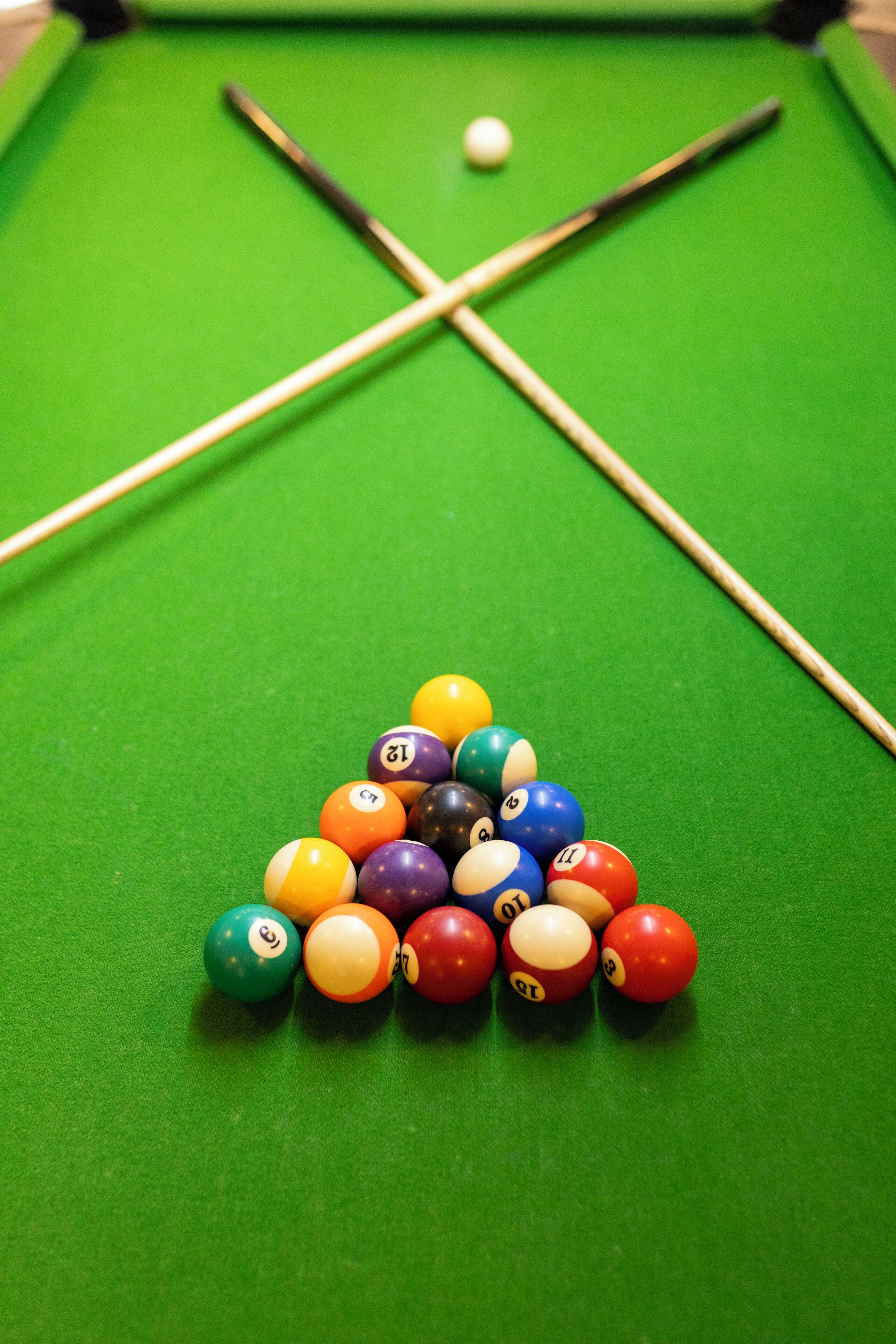 A pool table with a triangular arrangement of billiard balls and two pool cues.