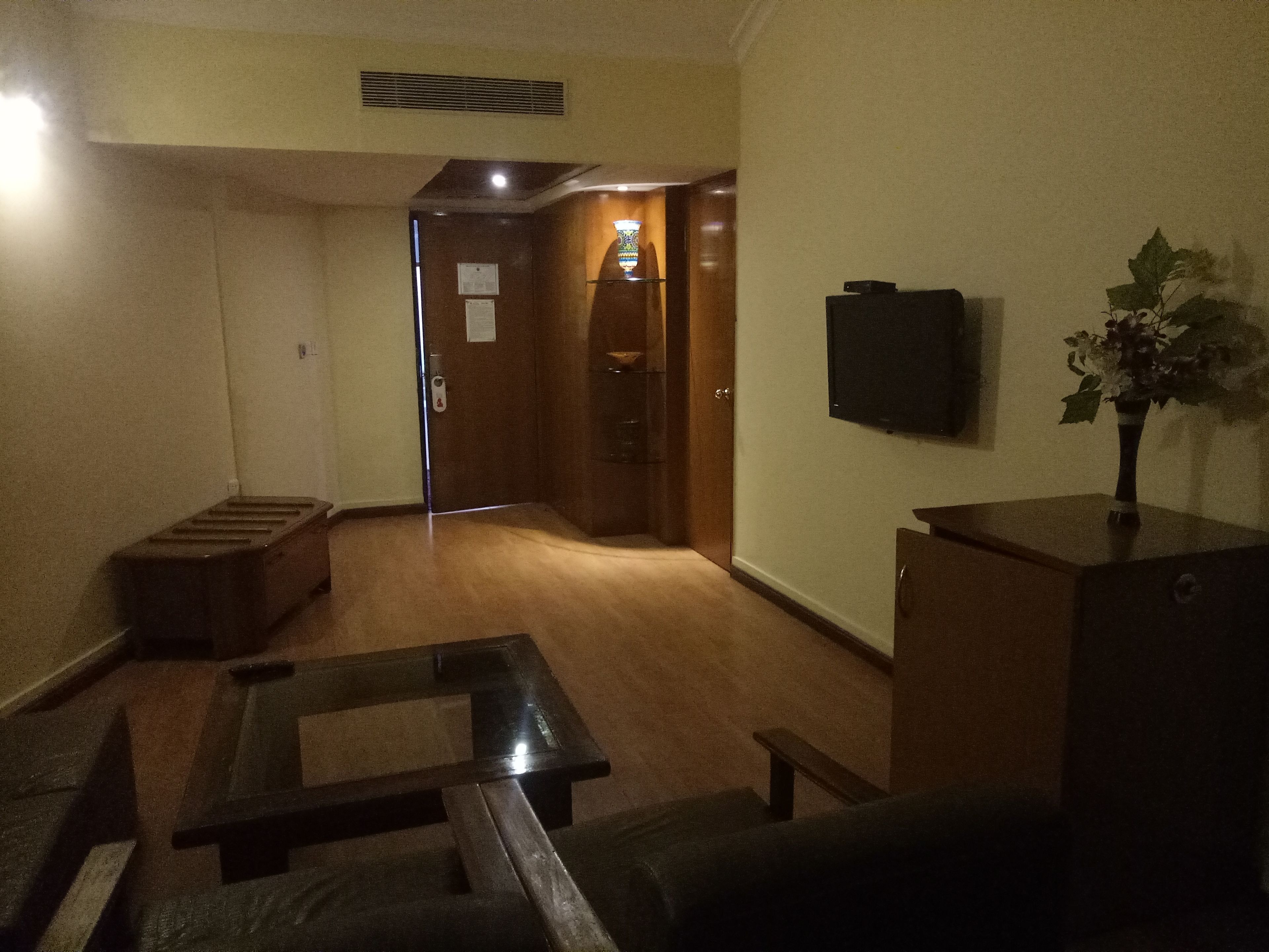 A dimly lit living room with a wooden bench, a small table, and a television mounted on the wall.