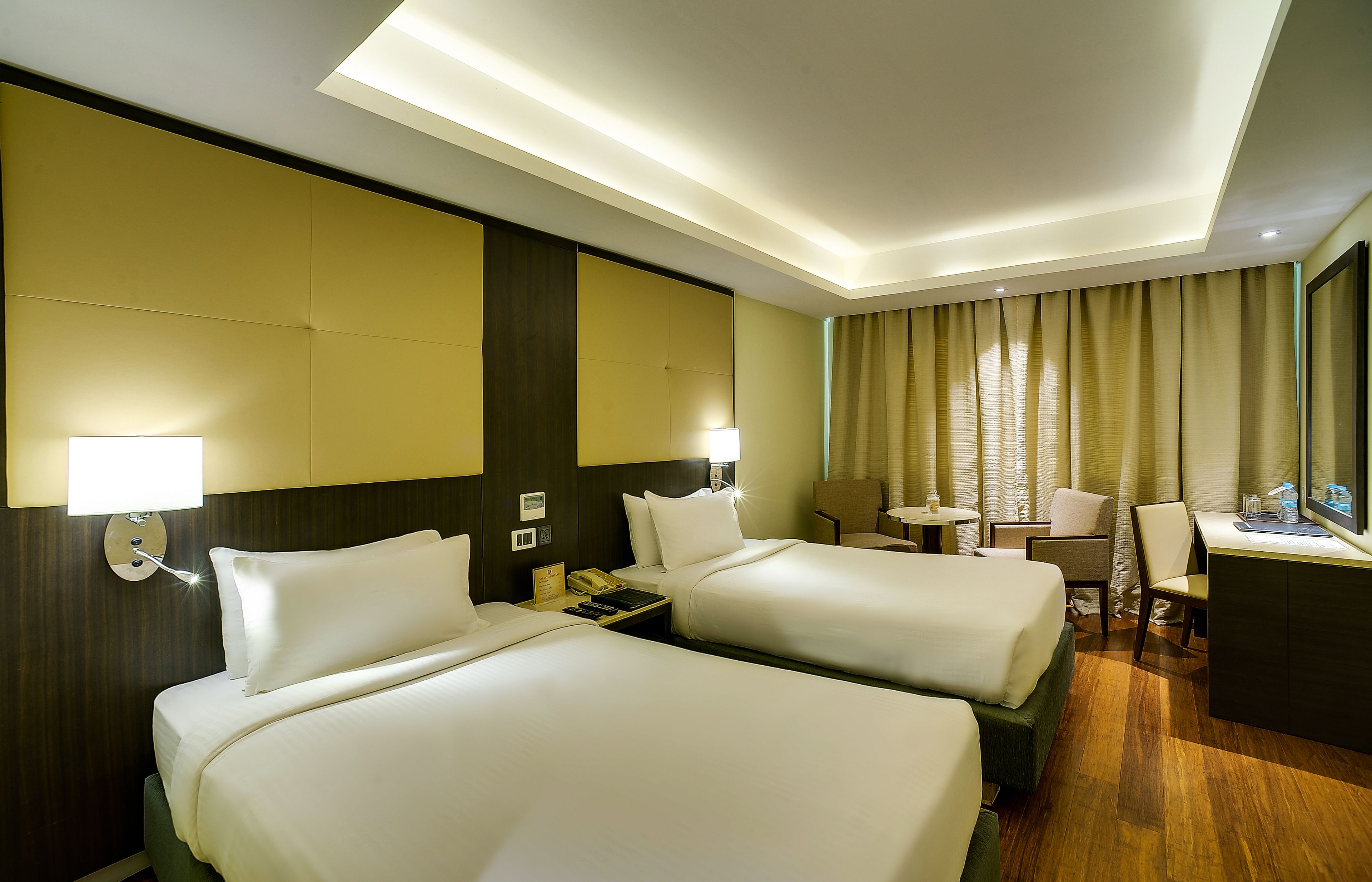 A hotel room with two beds, a desk, a chair, a small table, and a mirror.