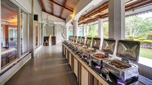 Zona de bufé con varias estaciones de comida, una escalera y grandes ventanales con vistas al exterior.