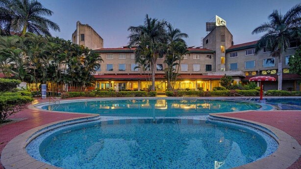 Un hotel con una amplia piscina central rodeada de palmeras y un camino de ladrillo rojo.