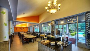 Un comedor amplio con varias mesas y sillas, una barra de buffet central y grandes ventanales con vistas al exterior.