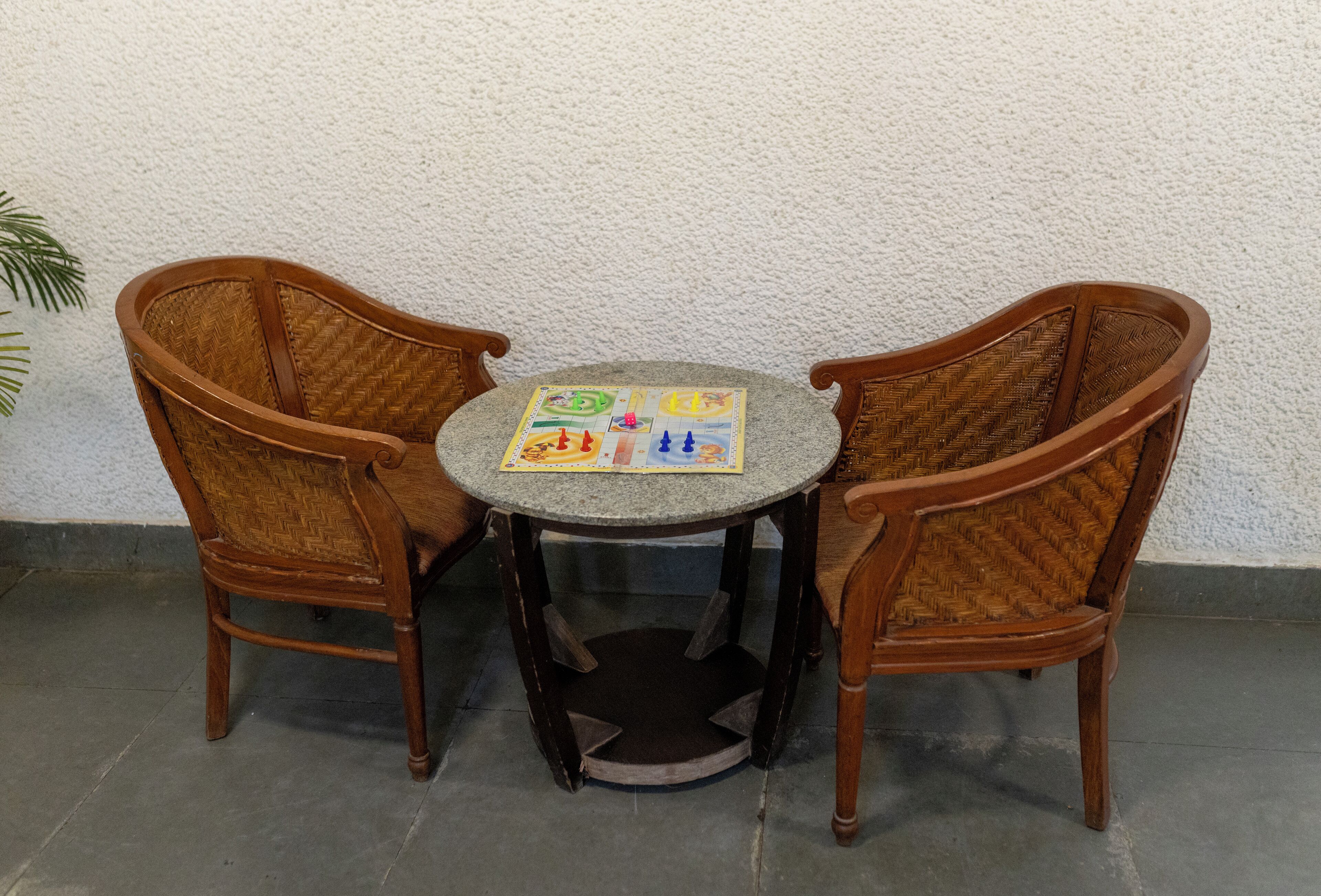 A round table with a woven chair on each side, a small rug, and a board game on the table.