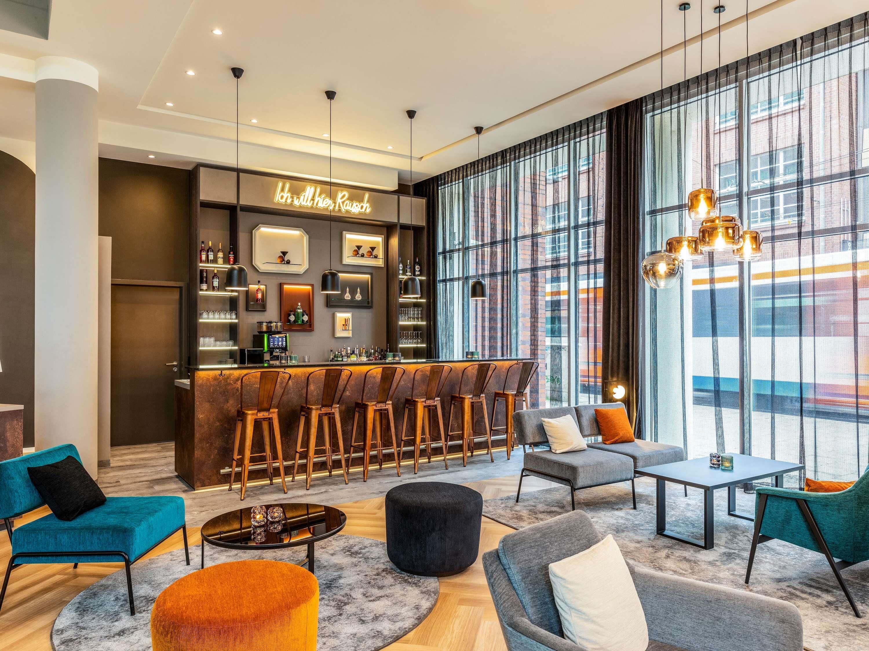 A modern bar area with a neon sign, bar stools, and a seating area with sofas and a table.