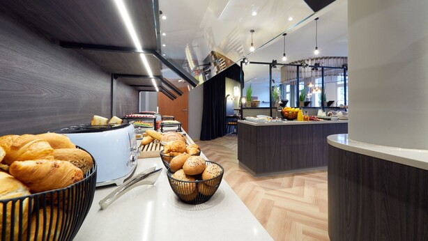 A modern kitchen with a buffet setup, including bread and pastries, and a counter with various food items. - ibis Styles Bielefeld (Bielefeld)