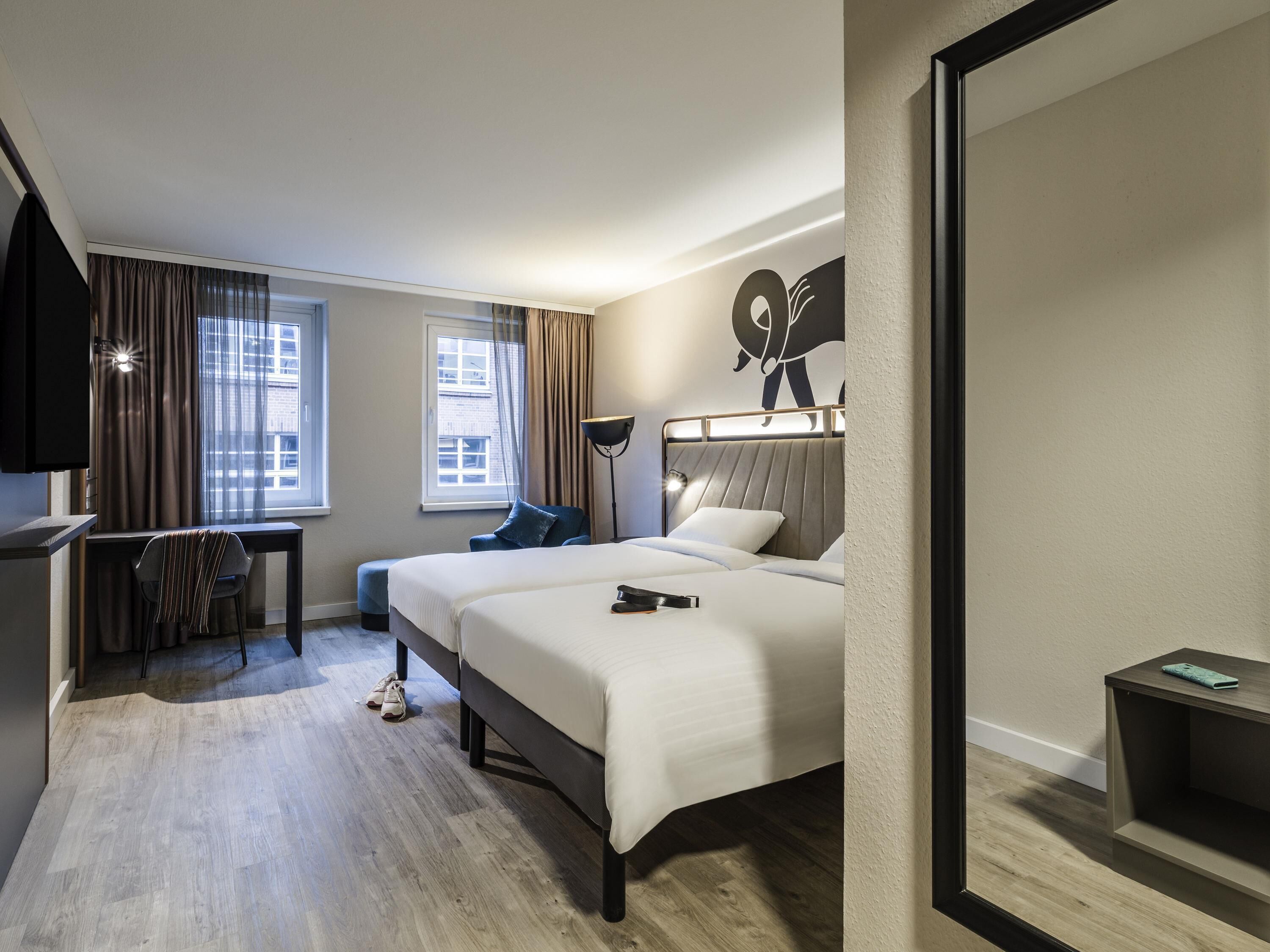 A hotel room with a bed, a desk, a chair, a TV, and a window.