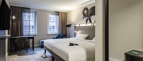 A hotel room with a bed, a desk, a chair, a TV, and a window.